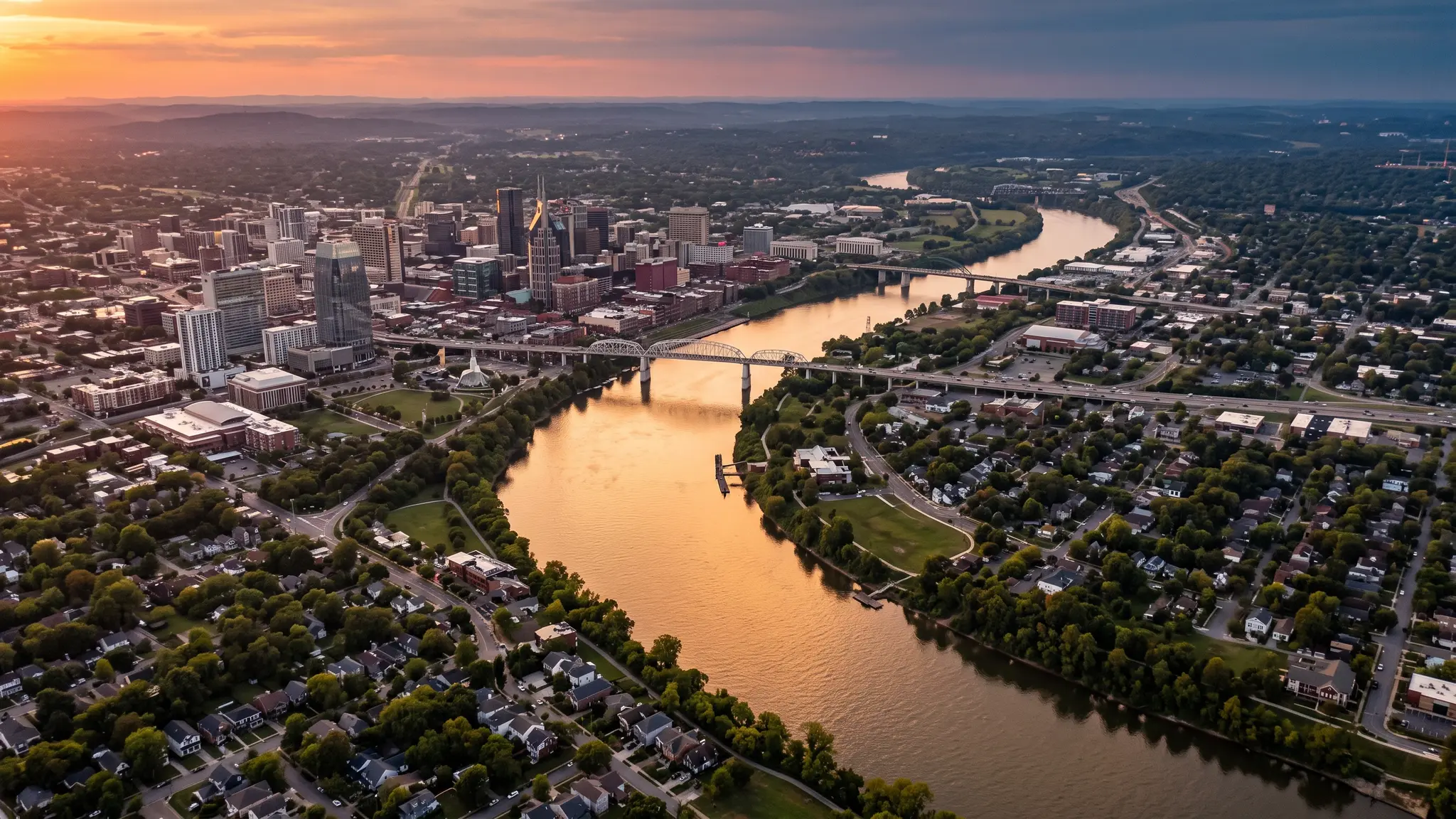 Aerial view of the Cumberland River winding past the Nashville skyline and residential neighborhoods at sunset